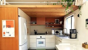 Een kleine keuken met houten kastjes, een koelkast, een magnetron en een koffiezetapparaat.
