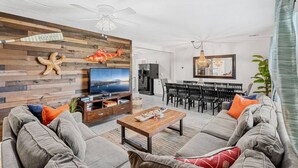 A living room with a TV, wooden wall decor, and a dining area with a chandelier.