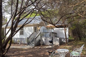 Une maison blanche avec un porche, un escalier et un barbecue dans la cour.