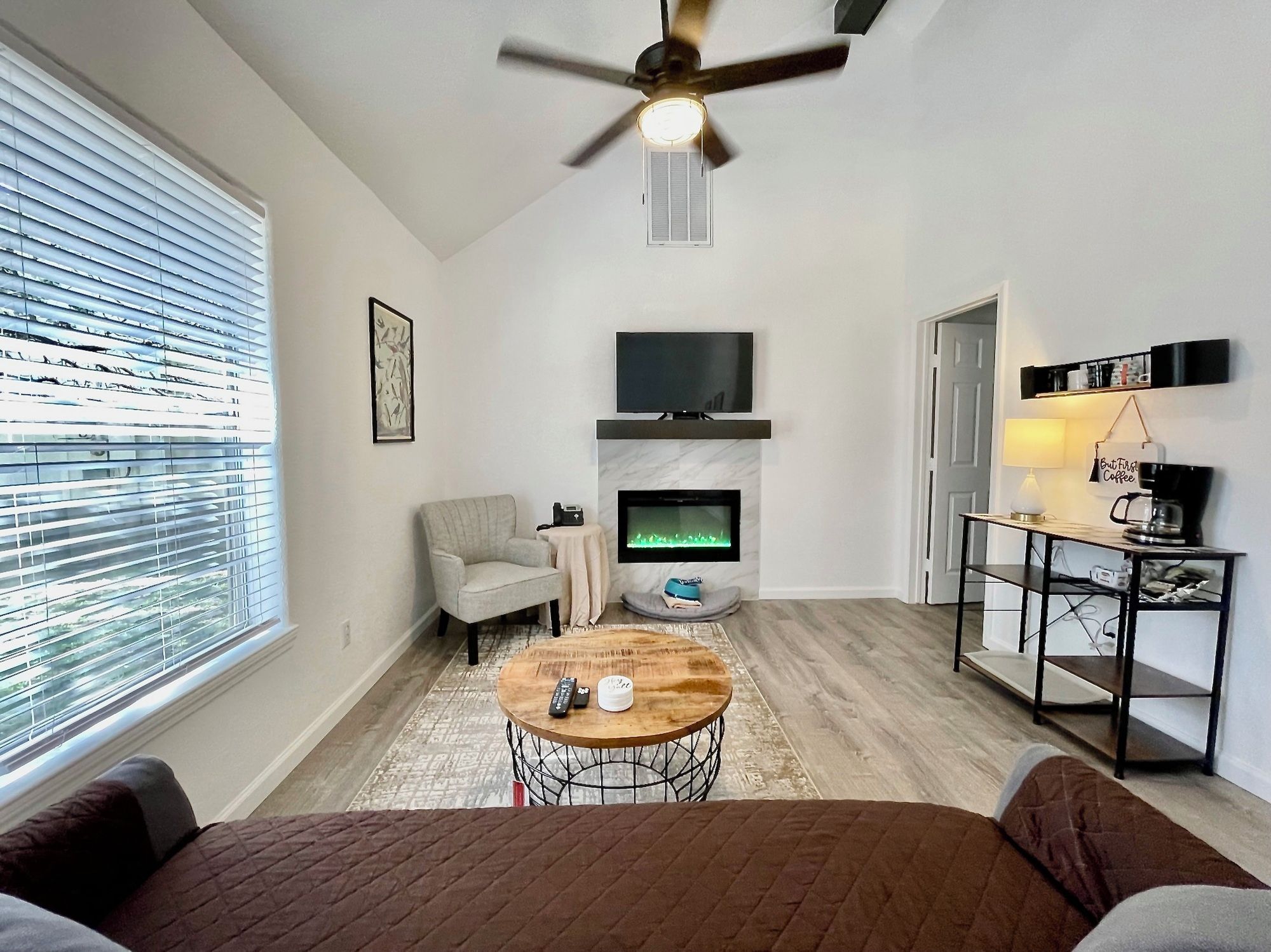 A modern living room with a fireplace, a television, a ceiling fan, and a coffee table.