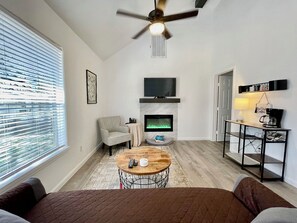 A modern living room with a fireplace, a television, a ceiling fan, and a coffee table.