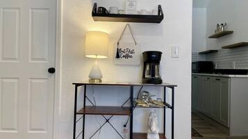 A kitchen area with a coffee maker on a shelf, a hanging sign with a coffee-related message, and a lamp on a table.