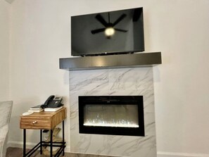 Un salon moderne avec une cheminée, un téléviseur fixé au mur et un téléphone posé sur une petite table en bois.