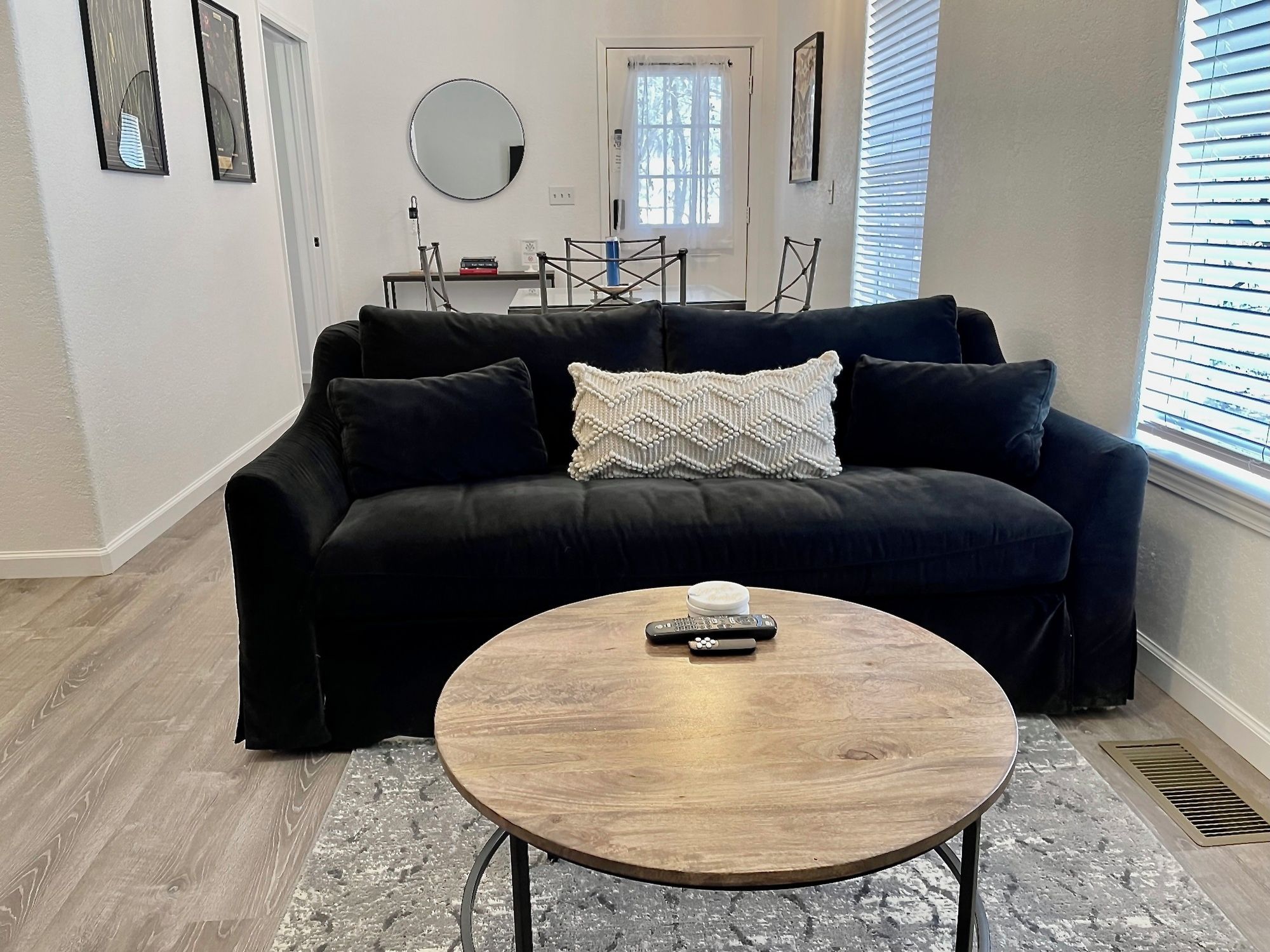 A living room with a black sofa, a round wooden coffee table, and a remote control on it.
