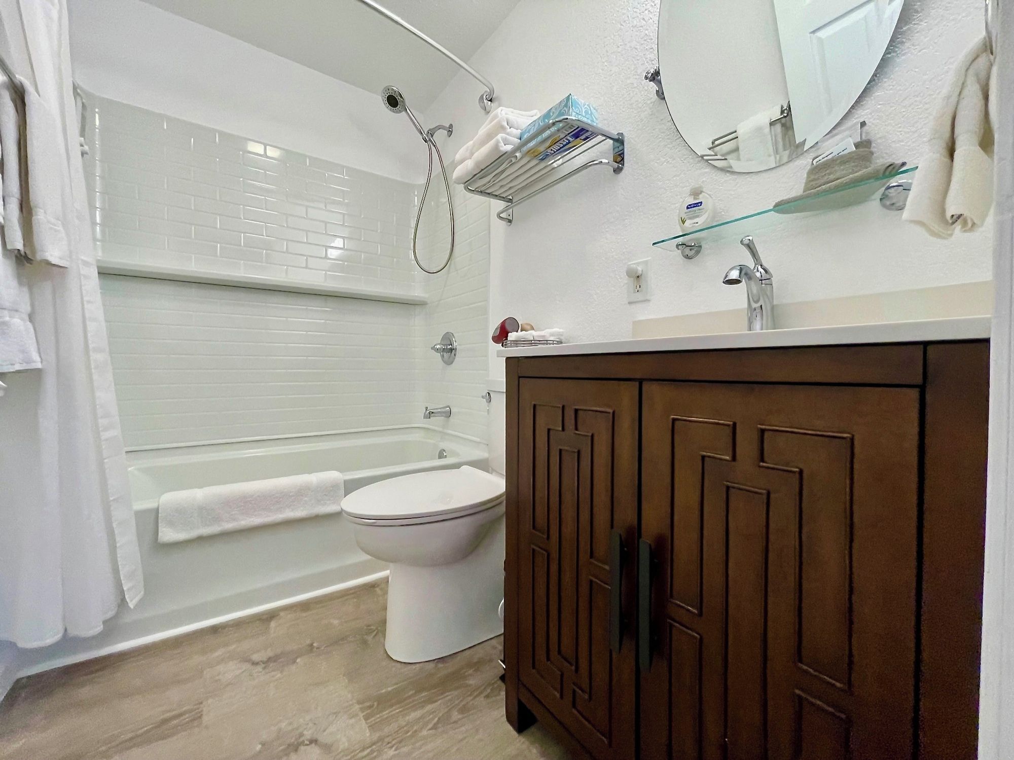 A bathroom with a white toilet, a bathtub, a shower, and a wooden vanity with a mirror.