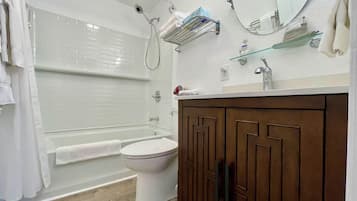 A bathroom with a white toilet, a bathtub, a shower, and a wooden vanity with a mirror.