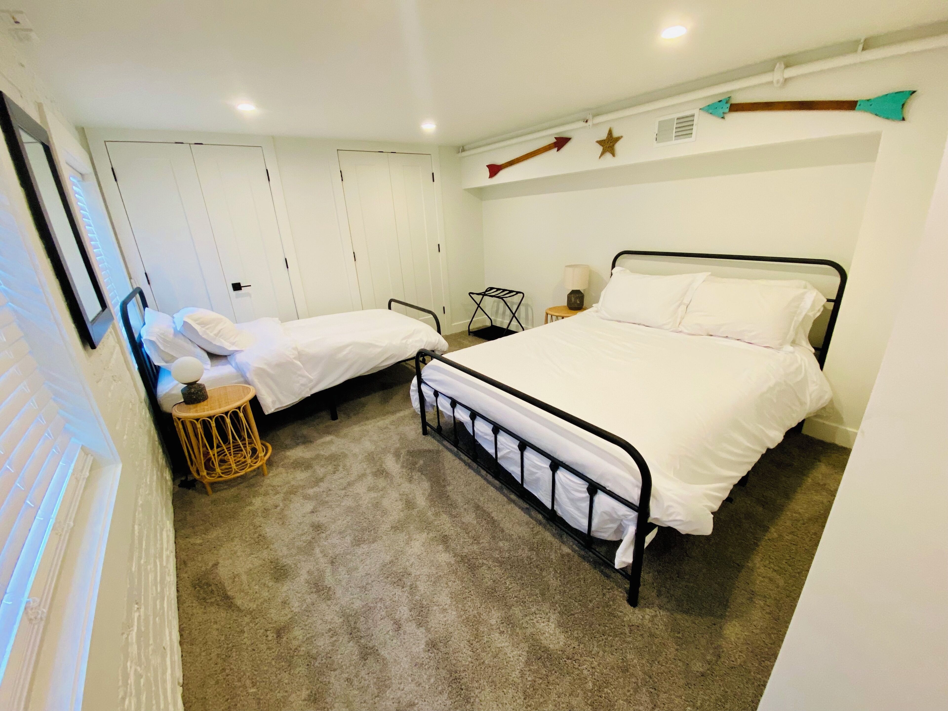 Un dormitorio con dos camas individuales, una mesita pequeña y una silla. Las paredes son blancas y el techo tiene iluminación empotrada.
