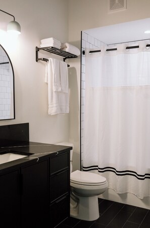 A bathroom with a black vanity, white toilet, and a shower curtain. - The Kroger Lofts (Charlevoix)