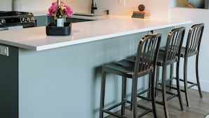A modern kitchen with a large island, bar stools, pendant lighting, and a brick wall. - The Kroger Lofts (Charlevoix)