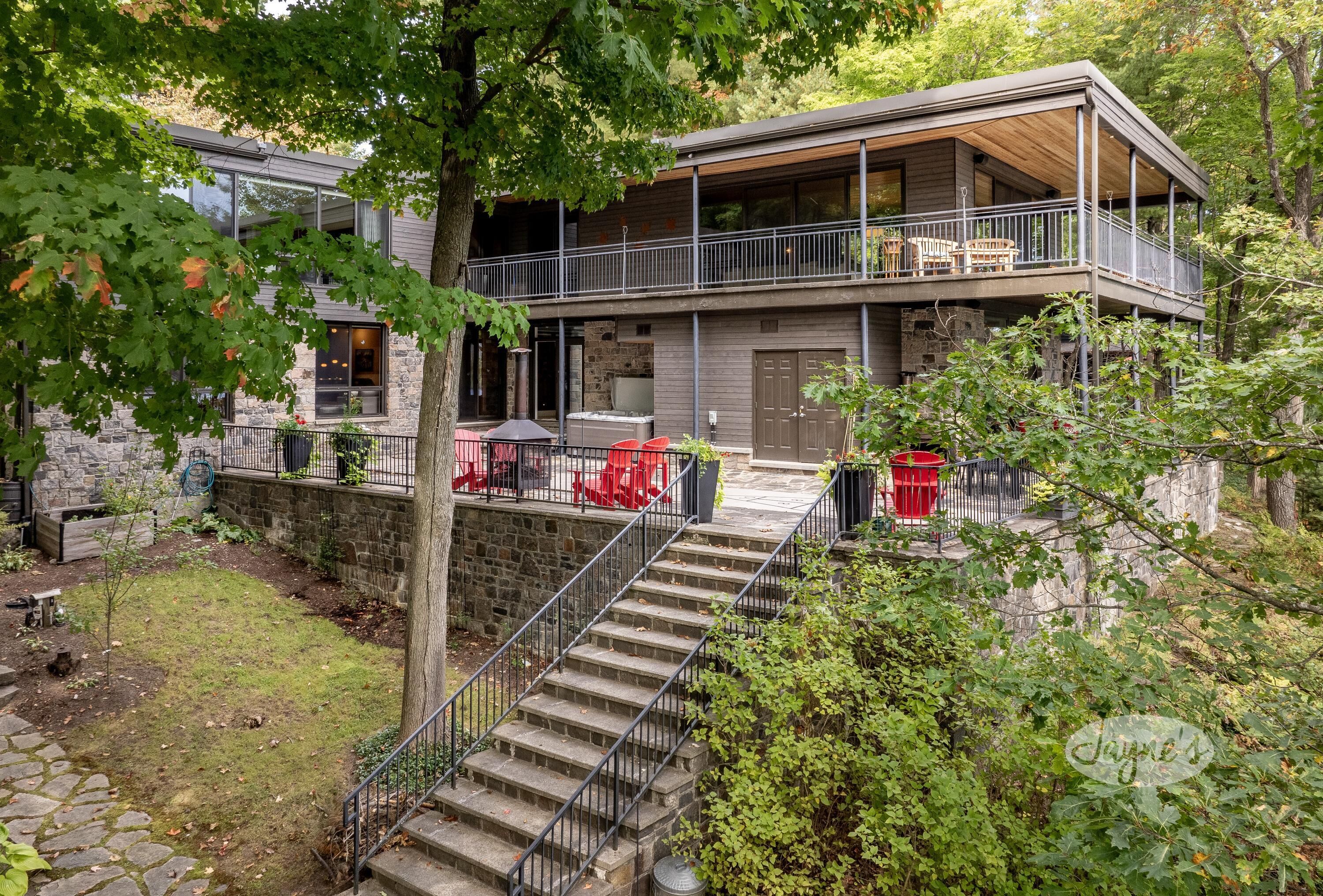 Ein modernes, zweistöckiges Haus mit einem Balkon, Steinmauern und einer Steintreppe, die zum Eingang führt.
