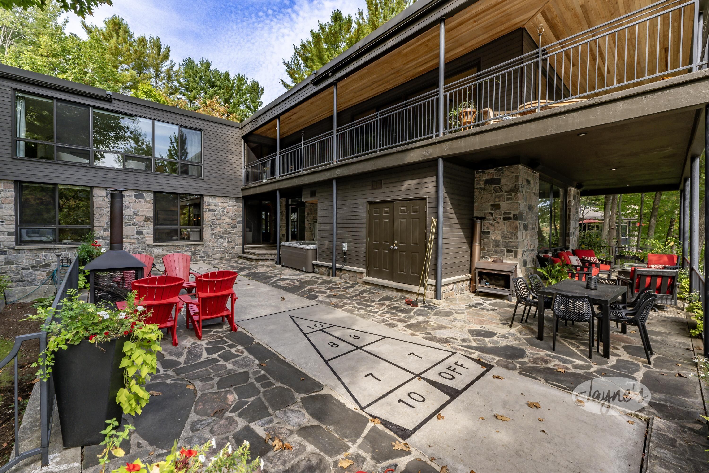 A modern outdoor patio with stone flooring, red chairs, and a shuffleboard game.