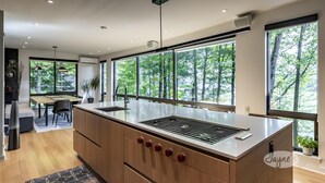 Una cocina moderna con una isla grande, electrodomésticos integrados y amplios ventanales con vistas a árboles.