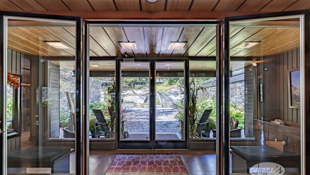 Una entrada moderna con puertas de vidrio, techo de madera y vistas a mesas al aire libre y vegetación.