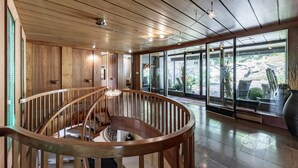 Un interior espacioso y moderno con una escalera de madera, ventanas grandes y vistas al exterior.