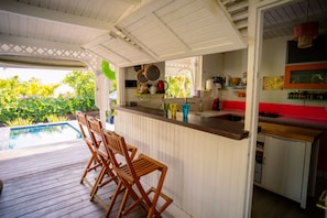 A kitchen with a bar area, wooden chairs, and a view of a swimming pool.