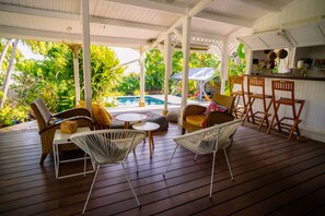 A covered outdoor area with wooden flooring, wicker furniture, and a pool.