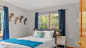 A bedroom with a bed, a nightstand, a window with curtains, and artwork on the wall. - Tranquil 3-bedroom house with a massage chair  (Springfield)