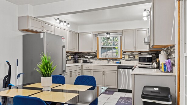 A modern kitchen with white cabinets, a dining area with blue chairs, and a small trash bin. - Tranquil 3-bedroom house with a massage chair  (Springfield)