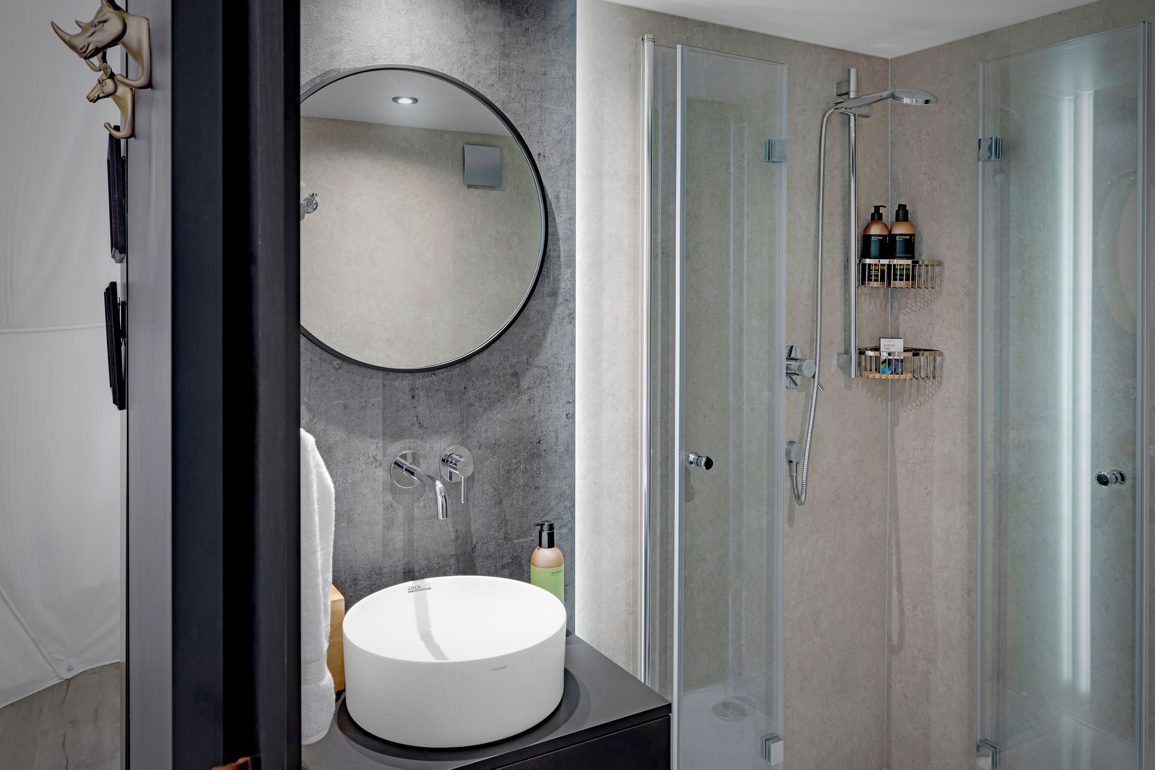 A modern bathroom with a round mirror, a white sink, and a glass-enclosed shower area.