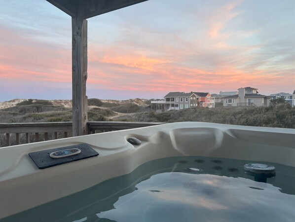 A hot tub with a wooden deck and a view of houses and dunes in the background.