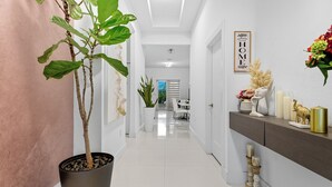 Un pasillo con una planta en maceta, un letrero que dice 'Welcome to Our Home' y una zona de comedor con sillas y una mesa.