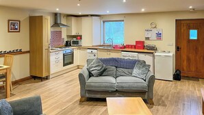 A compact living space with a kitchenette, a sofa, and a dining area. - Cooper Cottage - UK47544 (Potto, near Northallerton)