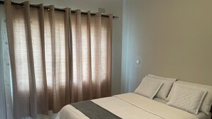 Een slaapkamer met een groot bed, beige gordijnen en een marmeren vloer.