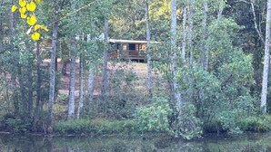 Une cabane entourée d’une forêt dense et bordant un lac paisible.