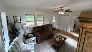 Un salon avec un canapé marron, un fauteuil à rayures, une petite table basse en bois sur laquelle est posé un vase, et un ventilateur de plafond.
