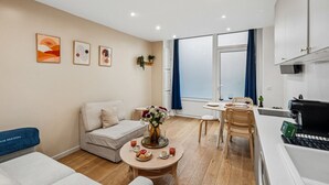 Ein modernes Wohnzimmer mit einer Couch, einem Esstisch mit Stühlen, einem Couchtisch und einer Küchenzeile mit Herd.