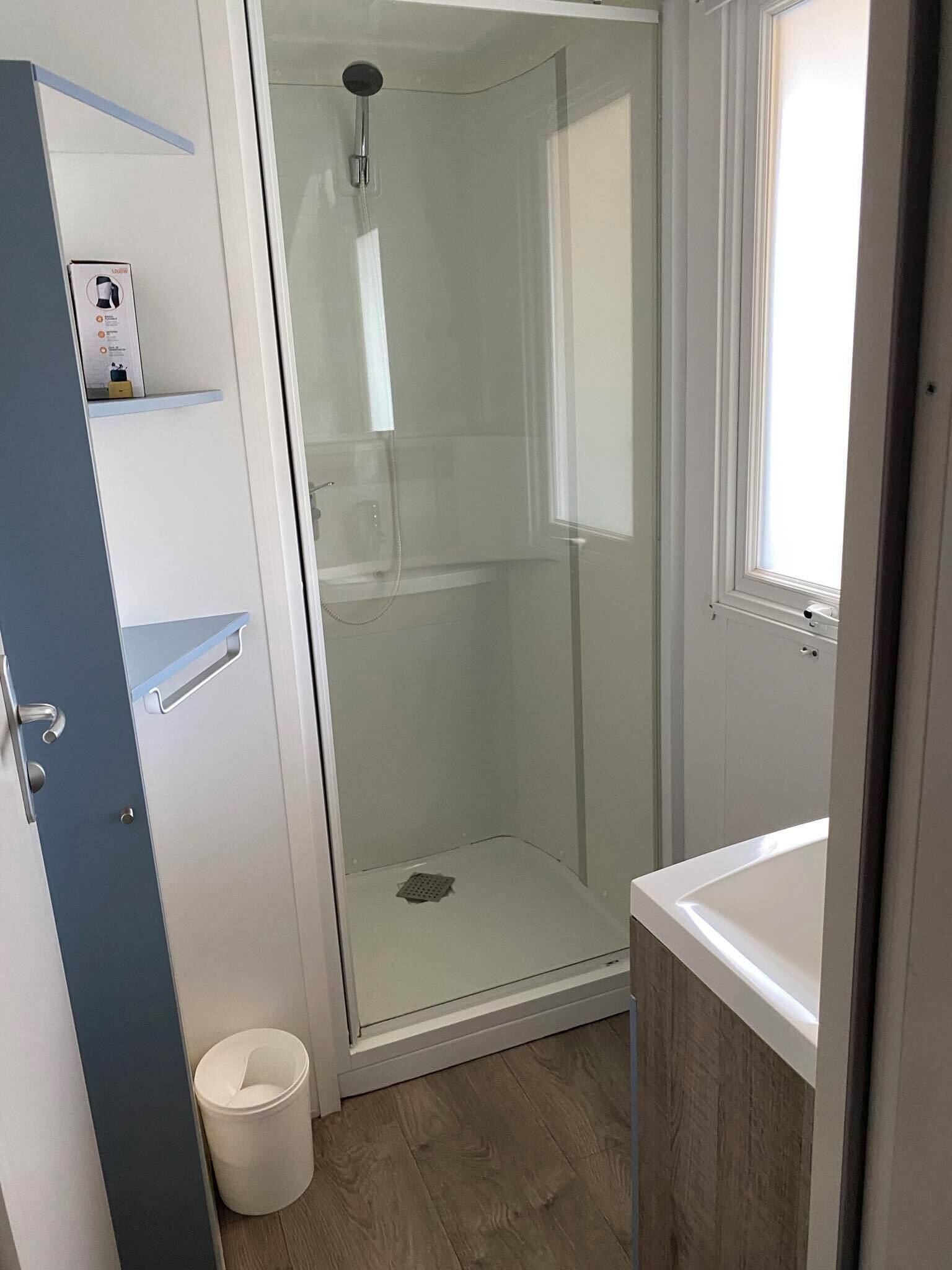 Un baño moderno con cabina de ducha de vidrio, un lavamanos blanco y suelo de madera.