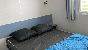 A single bed with a grey mattress and blue bedding, a small bedside table, and a wall-mounted shelf above the bed.
