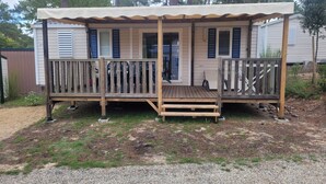 A mobile home with a wooden deck, two doors with shutters, and a covered porch.