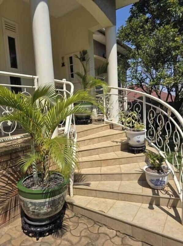Staircase leads to a classic building entrance, flanked by lush greenery and white railings.