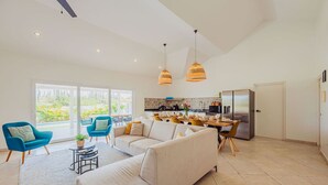 A spacious living area with a sofa, chairs, a dining table, and a kitchen in the background.