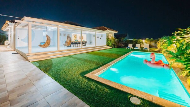 A modern house with a glass-enclosed patio, a swimming pool, and outdoor seating.