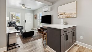 A modern kitchen with a flat-screen TV, a large window, and a dining area with a table and chairs. - Beach 5 Villas - Immaculate 300 steps from the Ocean (Fernandina Beach)