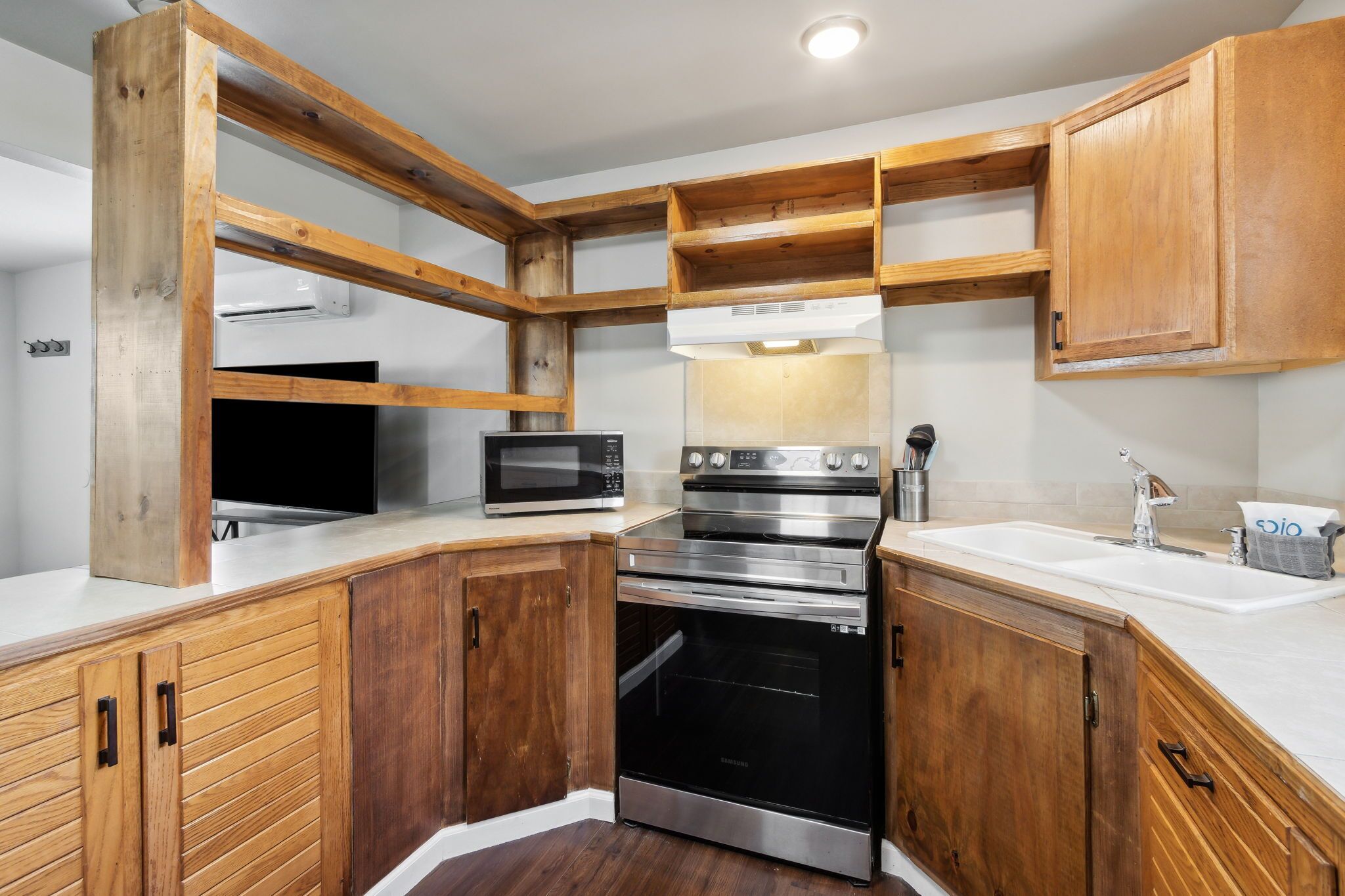 Una cocina con armarios de madera, horno de acero inoxidable, microondas y un lavamanos.