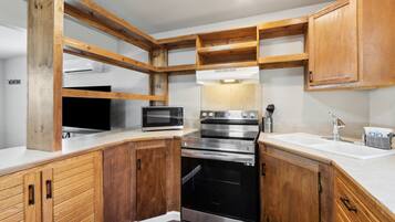 Una cocina con armarios de madera, horno de acero inoxidable, microondas y un lavamanos.