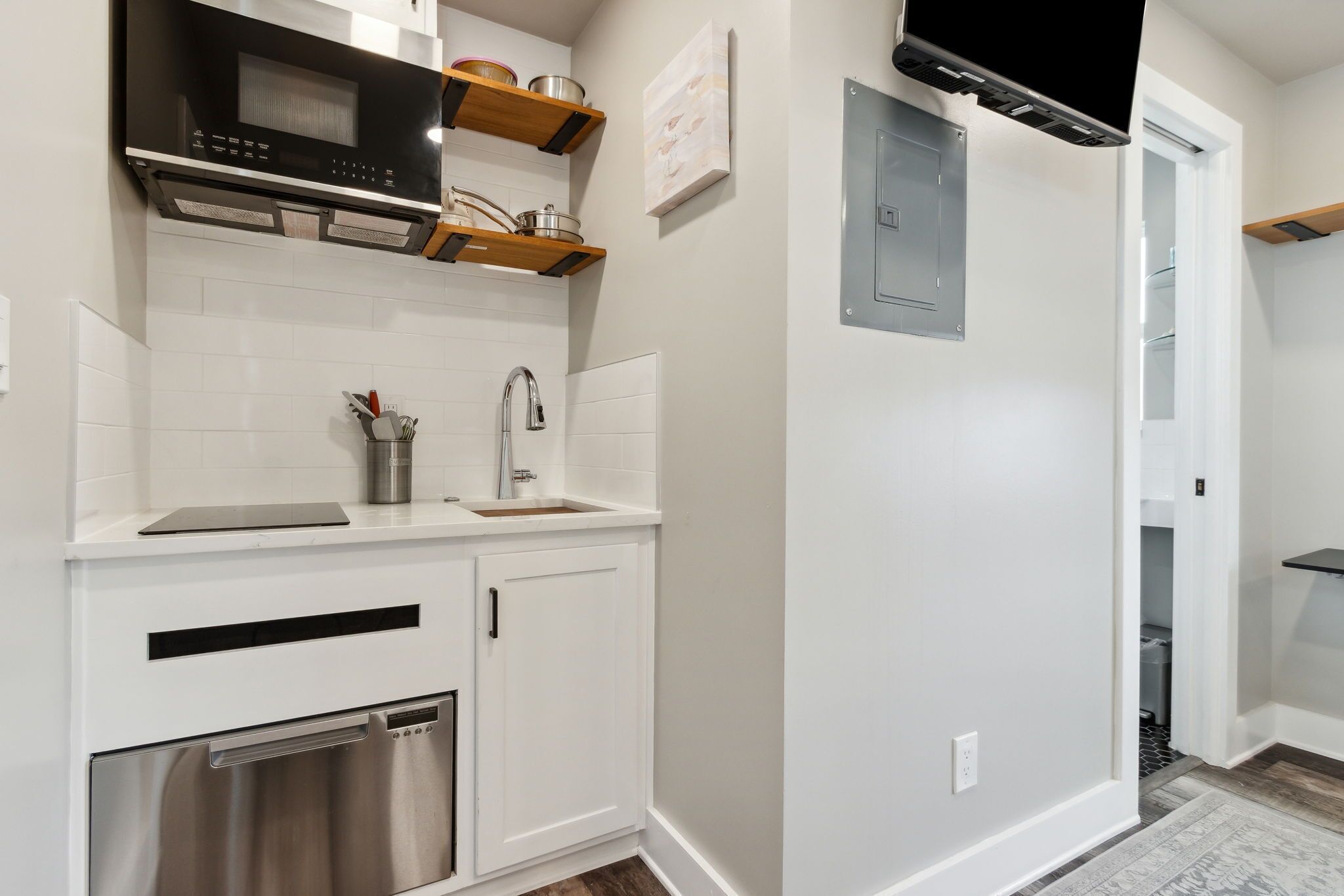Una cocina moderna con armarios blancos, lavavajillas de acero inoxidable, microondas y estantes de madera sobre la encimera.