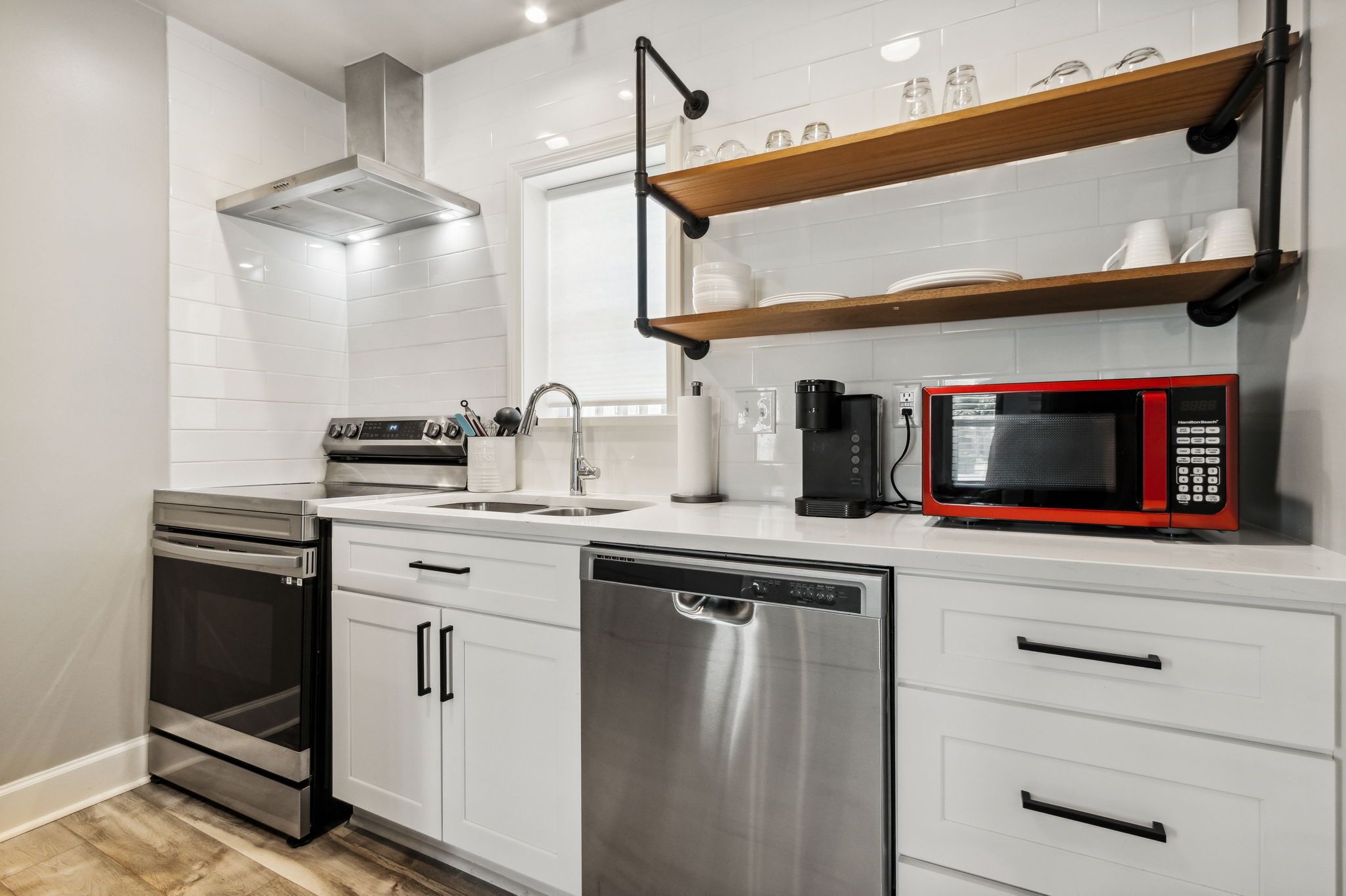 Una cocina moderna con electrodomésticos de acero inoxidable, armarios blancos y repisas de madera sobre la encimera.