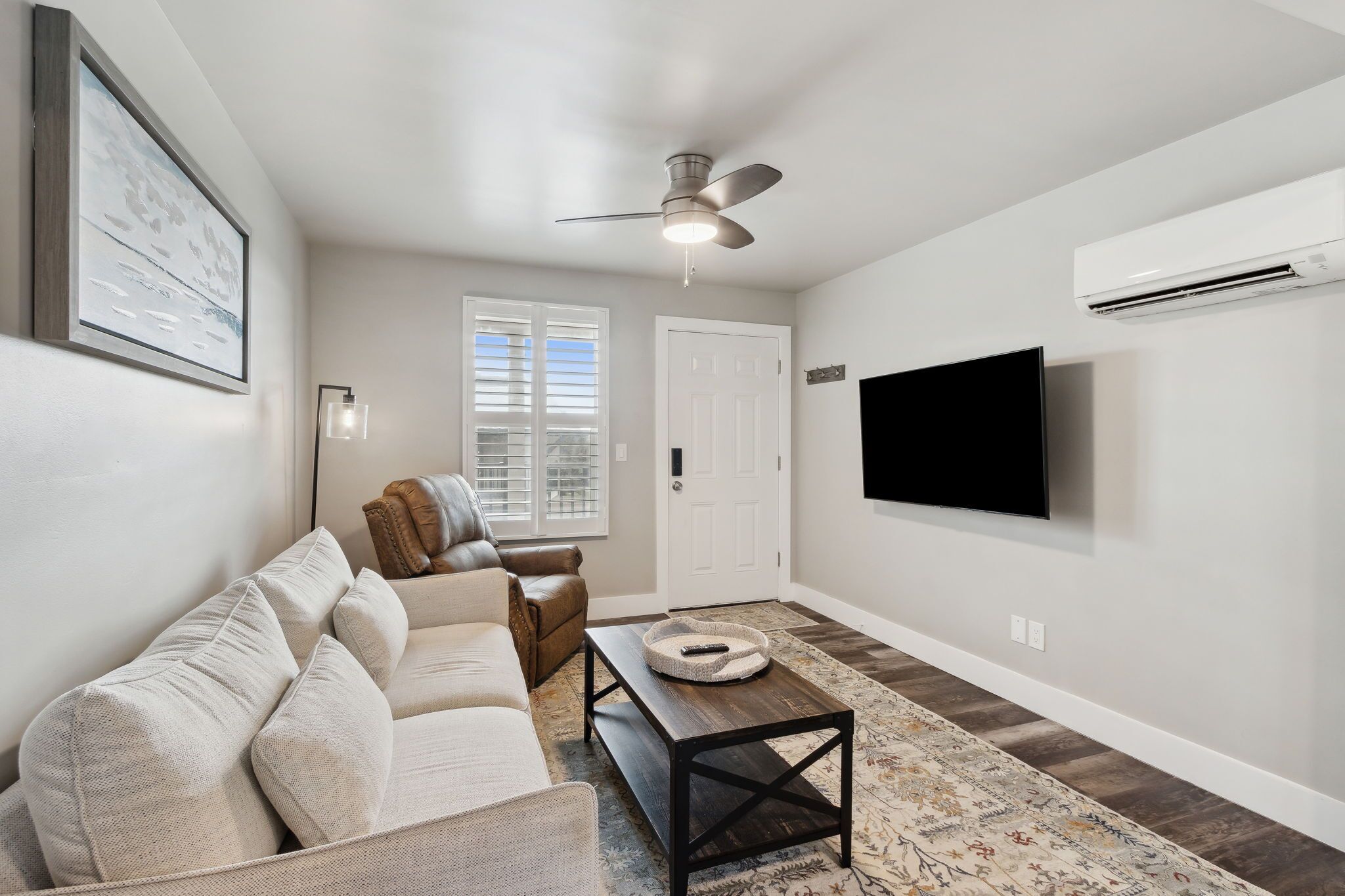 A living room with a sofa, a coffee table, a ceiling fan, a TV, and an air conditioning unit.