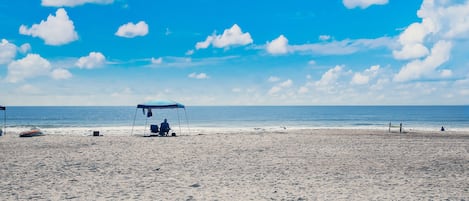 A beach with a covered seating area and a volleyball net.