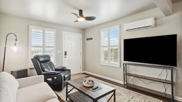 A living room with a leather recliner, a coffee table with a bowl, a flat-screen TV on a metal stand, and a ceiling fan.