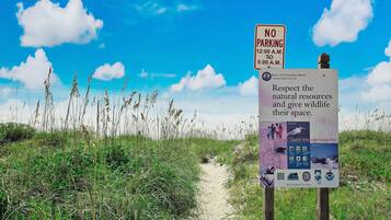 Un sentier menant à la plage, agrémenté d’un panneau indiquant « Stationnement interdit » et d’un autre rappelant l’importance de respecter les ressources naturelles.