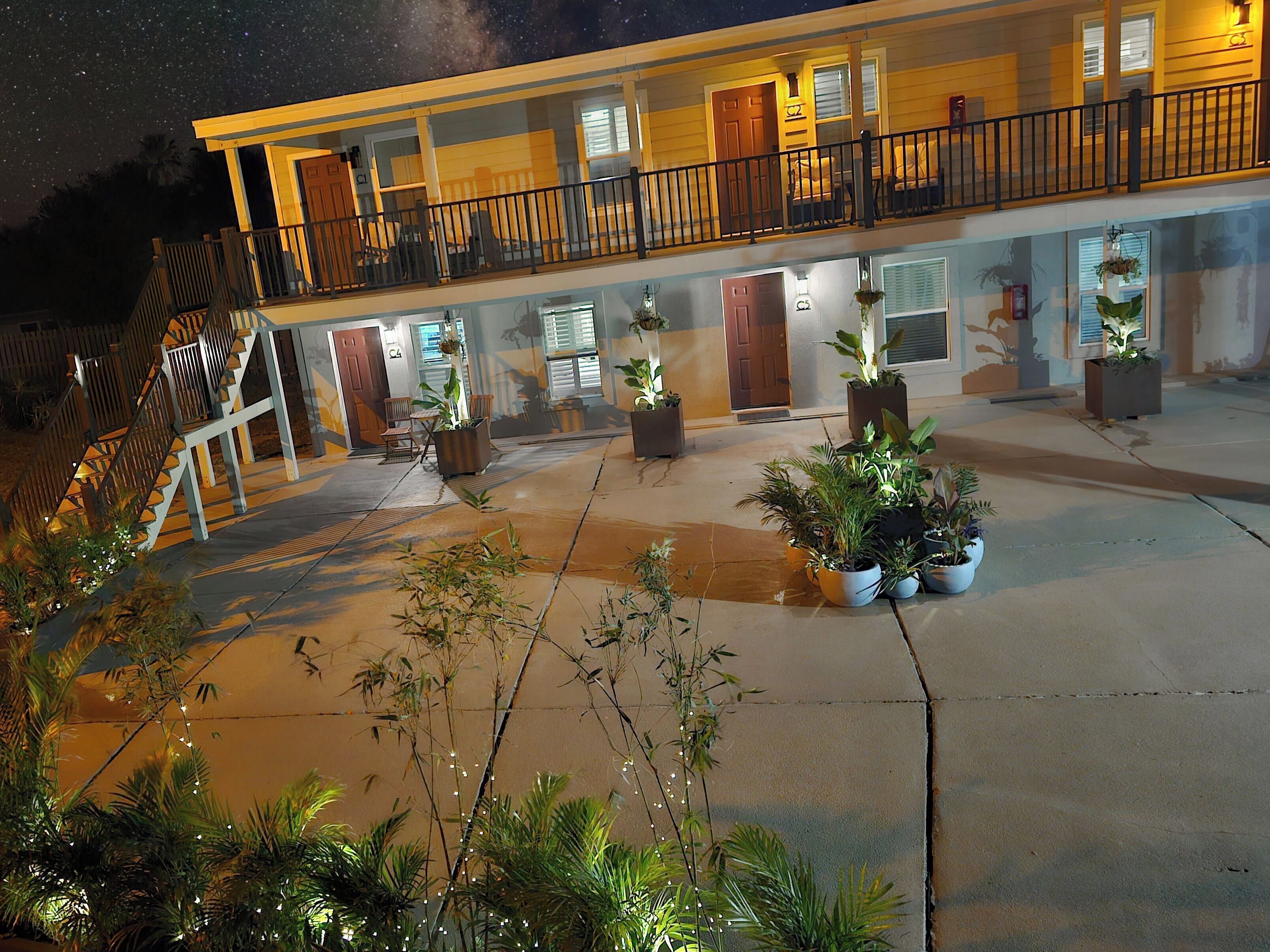 A motel with a balcony, outdoor seating, and potted plants.