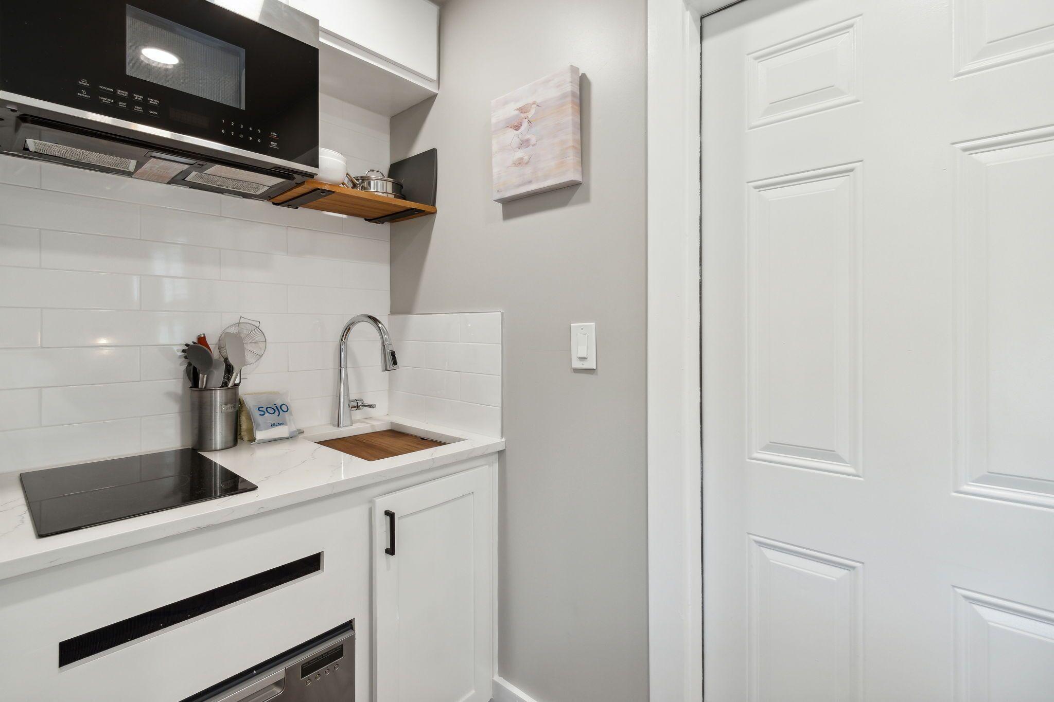 Une cuisine moderne avec des meubles blancs, une plaque de cuisson à induction noire, un évier en acier inoxydable et un plan de travail en bois.