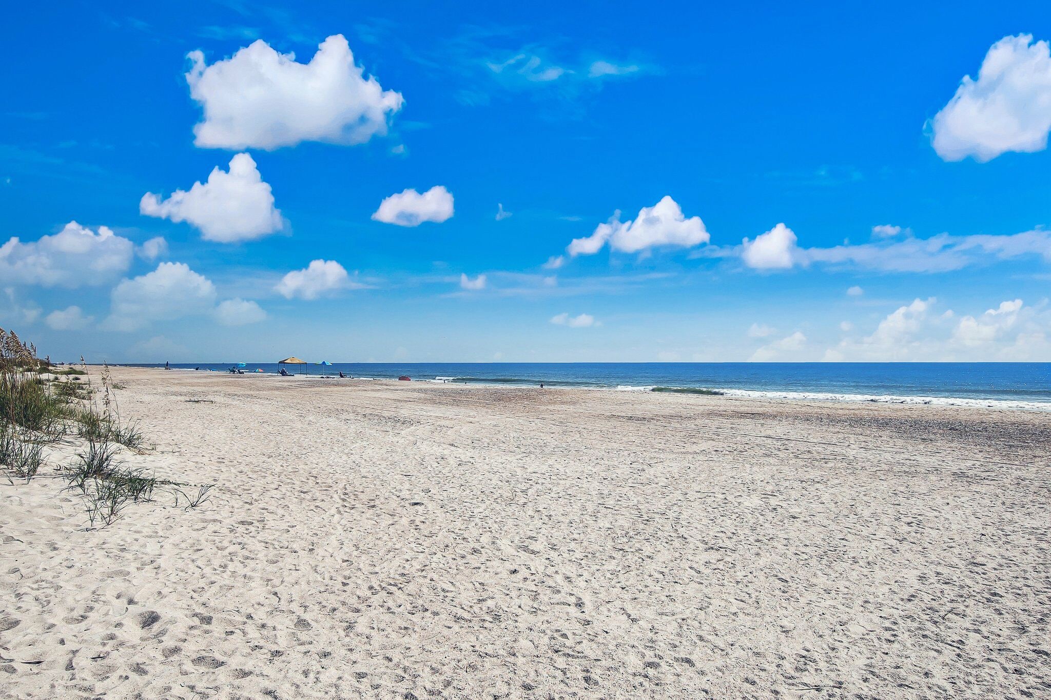 A wide sandy beach with a clear blue sky and ocean in the background.