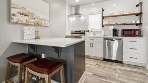 A modern kitchen with white cabinetry, a stainless steel dishwasher, a red microwave, and a wooden island with two stools. - Beach 5 Villas - Immaculate 300 steps from the Ocean (Fernandina Beach)