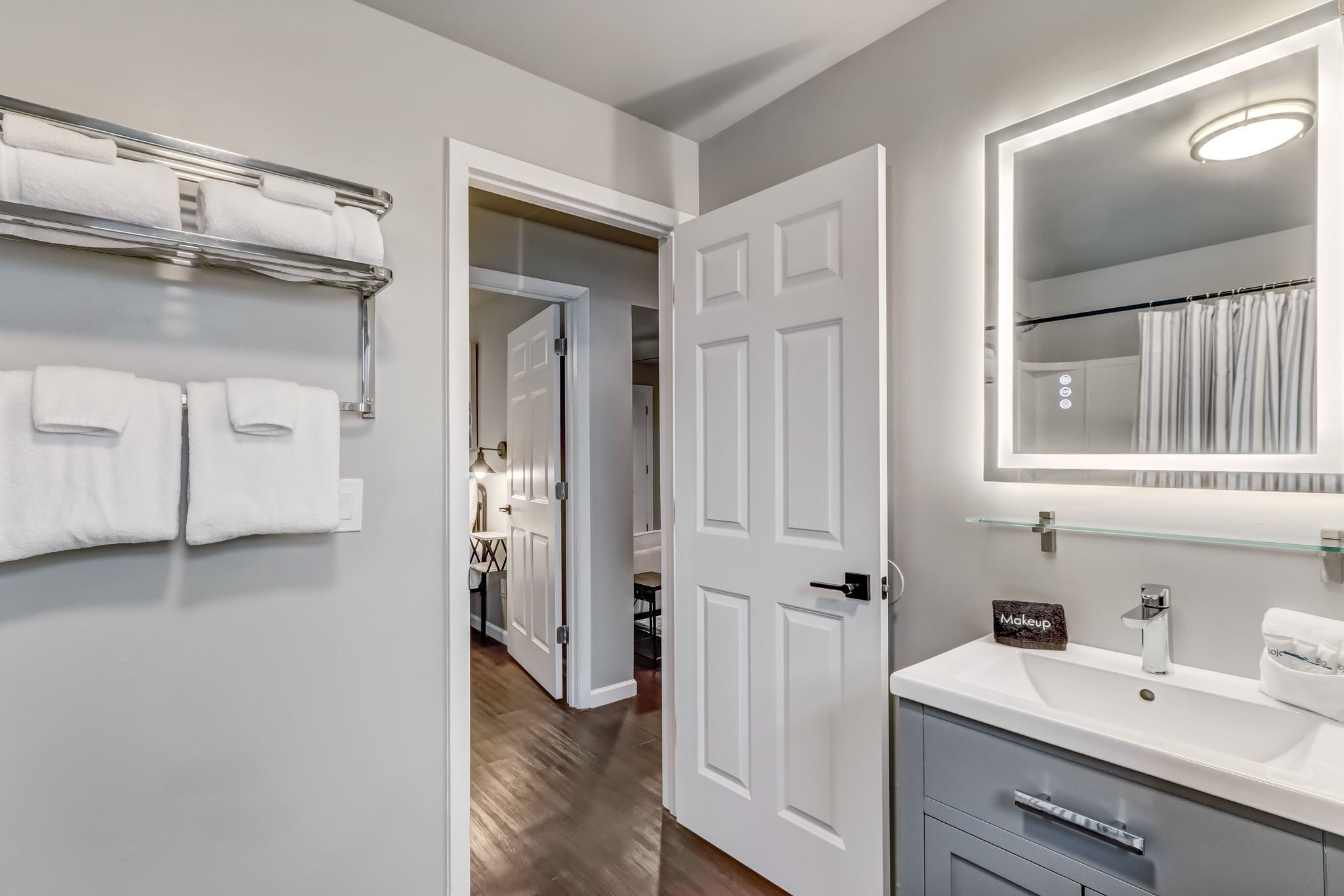 A modern bathroom with a white vanity, a glass shower enclosure, and a towel rack with neatly folded towels.